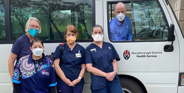 Four healthcare workers dressed in blue uniforms and front of bus with a driver in the front seat.