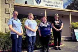 Four female nurse practitioners standing side by side in front of the garden at the main entrance to Maryborough Hospital.