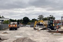 Works are in progress to develop a car park next to the hospital. There is a pile of earth in the foreground while a digger and truck are at rest.