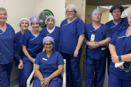 A group of theatre nurses, scrub scouts and technicians. They are wearing dark blue scrubs and smiling.