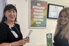 Two woman standing in front of a gender-inclusive sign with childbirth education posters.