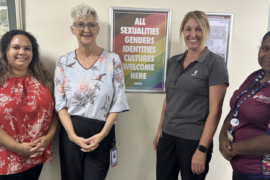 Four female health professionals stand in a row, in front of a gender inclusive sign.