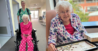 Left - a nurse pushes on older female patient in a wheel chair in the corridor of a hospital. Right - the smiling patient is settled in a new hospital room. She is wearing a dressing gown and doing a jigsaw puzzle.