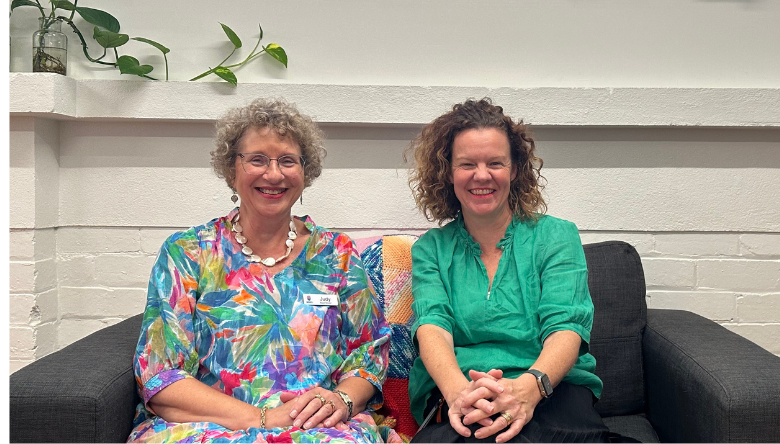 Two female leaders at a health service sit on a couch smiling