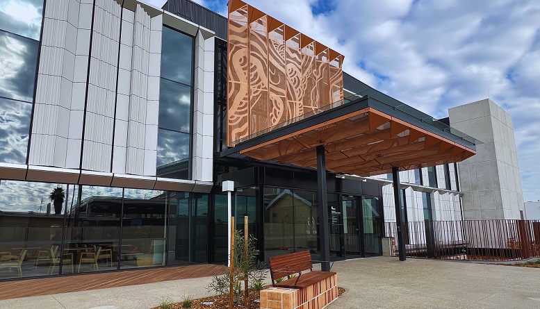 The main entrance to a new hospital. There is a large canopy over the doors and a seat in the forecourt.