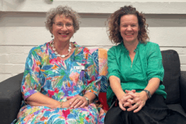 Two female leaders, a CEO and Board Chair, share a moment of connection on a couch. ‘Get involved’ is displayed in white font on an orange box in the top left.”