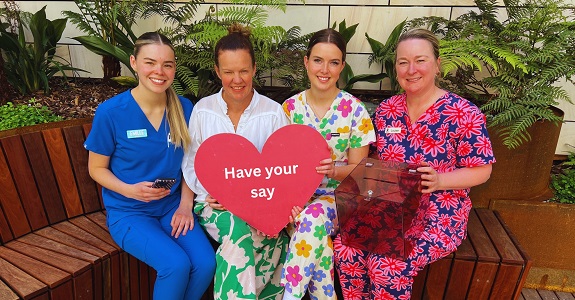 A health service CEO and three nurses in coloured scrubs sit in a courtyard.
