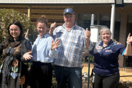 Four people standing in a garden with hands in air.