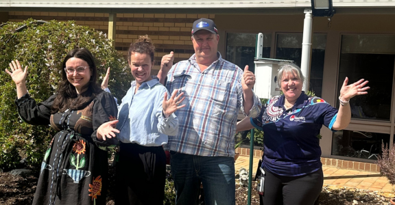 Four people standing in a garden with hands in air.
