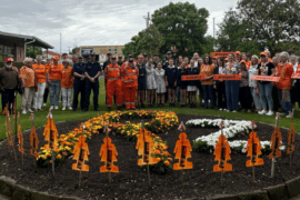 Big group of people standing behind a flower bed