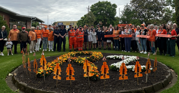 Big group of people standing behind a flower bed